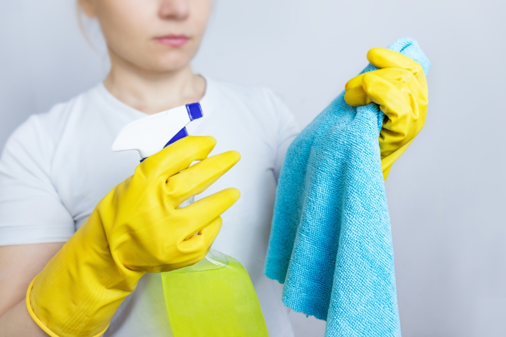 A woman spraying cleaning solution directly onto a microfiber cloth.